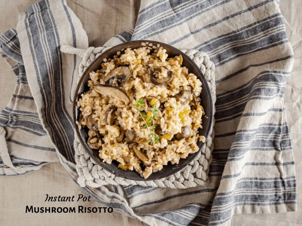 Top-down view of a bowl of mushroom risotto topped with a sprig of fresh thyme sitting on a blue striped towel. The title banner \"Instant Pot Mushroom Risotto\" appears in the left bottom corner.