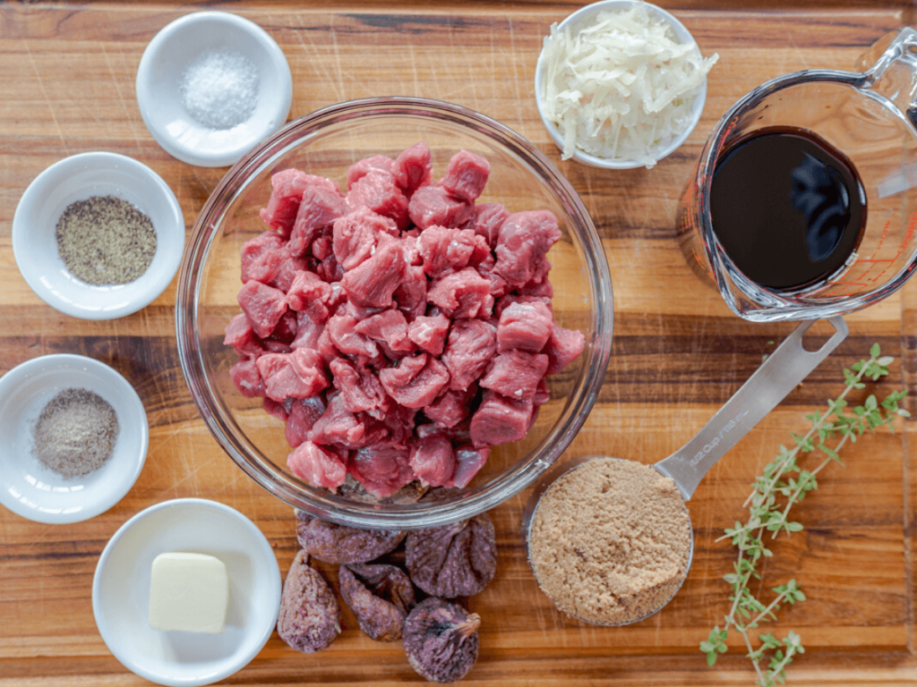 Top down view of ingredients to make lamb bites with fig balsamic glaze including lamb, brown sugar figs, thyme, pecorino cheese, balsamic vinegar, butter, salt, pepper and cardamon.