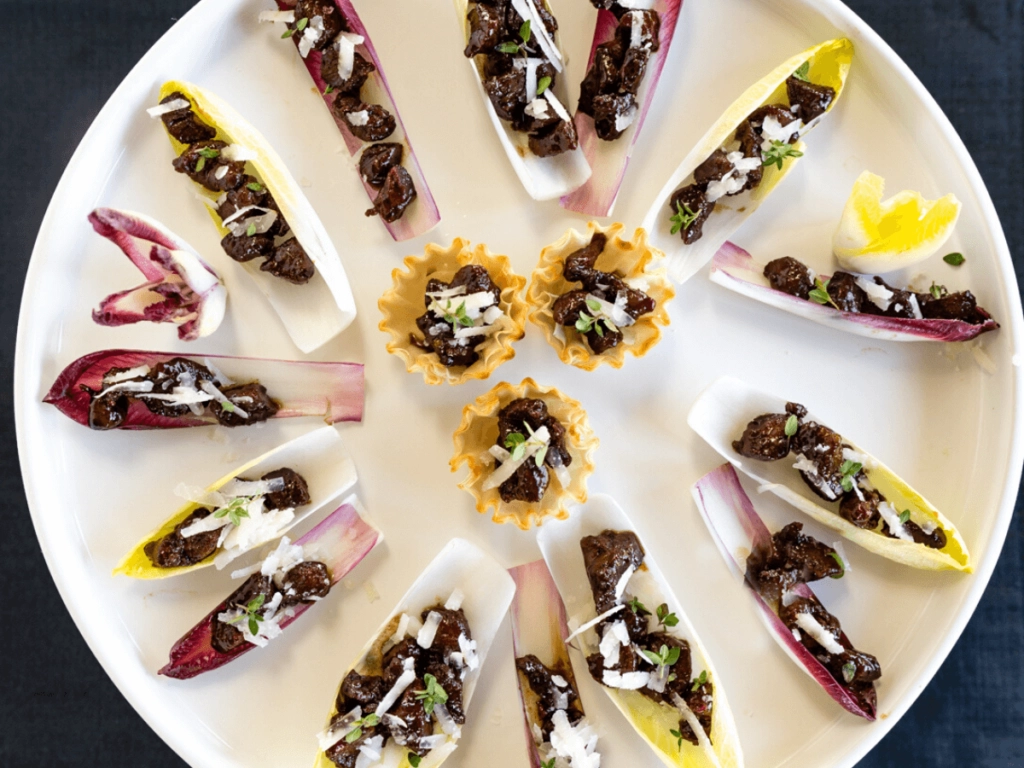 Top view of a round white platter filled with endive lettuce leaves and phyllo cups filled with lamb bits, pecorino cheese and fresh thyme