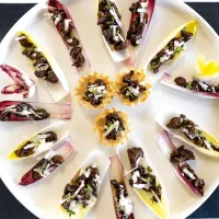 Top view of a round white platter filled with endive lettuce leaves and phyllo cups filled with lamb bits, pecorino cheese and fresh thyme