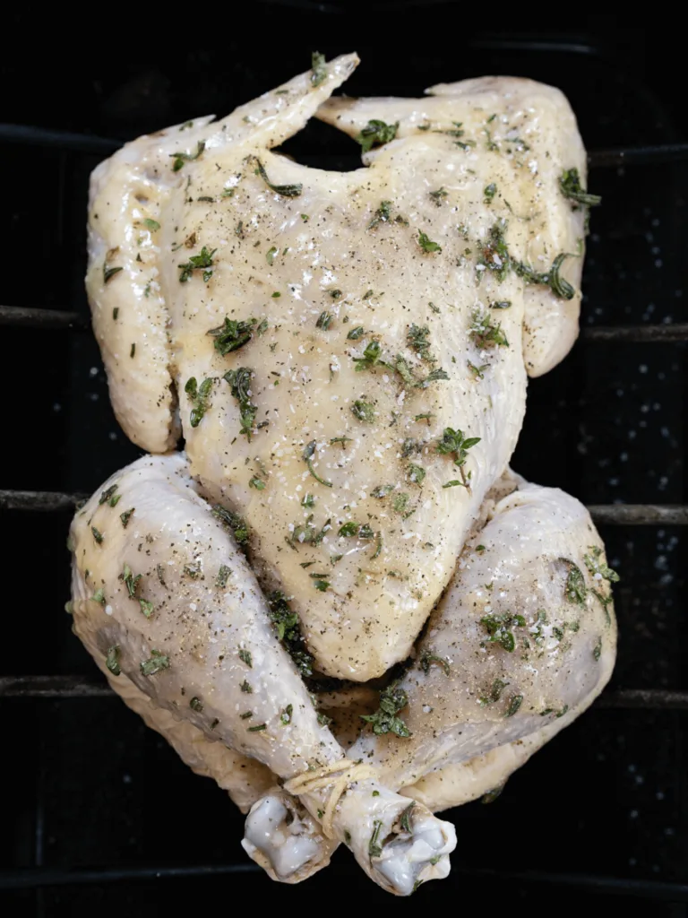 Uncooked whole chicken rubbed with fresh thyme and butter with the legs trussed with string.