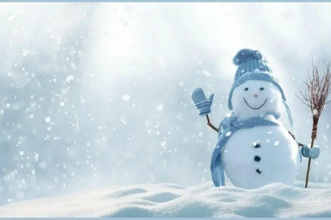 Photo of a snowman dressed in a blue hat, gloves, and a scarf holding whisk broom and standing in the snow with a smile on his face.