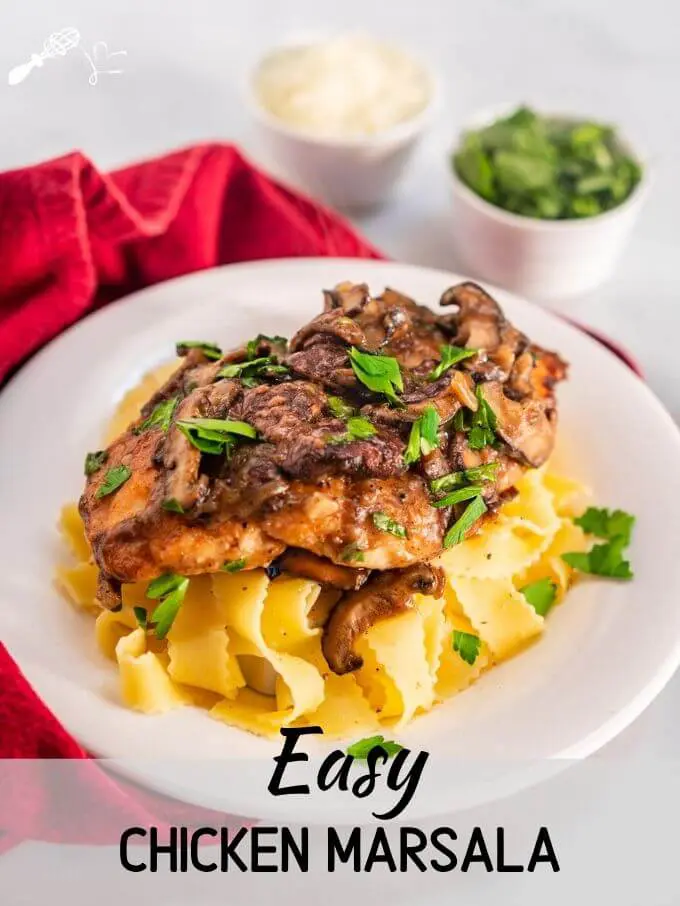 Angled view of a dish of browned chicken breasts on a bed of egg noodle pasta covered with a creamy mushroom marsala sauce and garnished with parsley in a white bowl sitting on a red napkin. Small dishes of parsley and cheese in the background and the title banner \"Easy Chicken Marsala Recipe\" runs across the bottom.