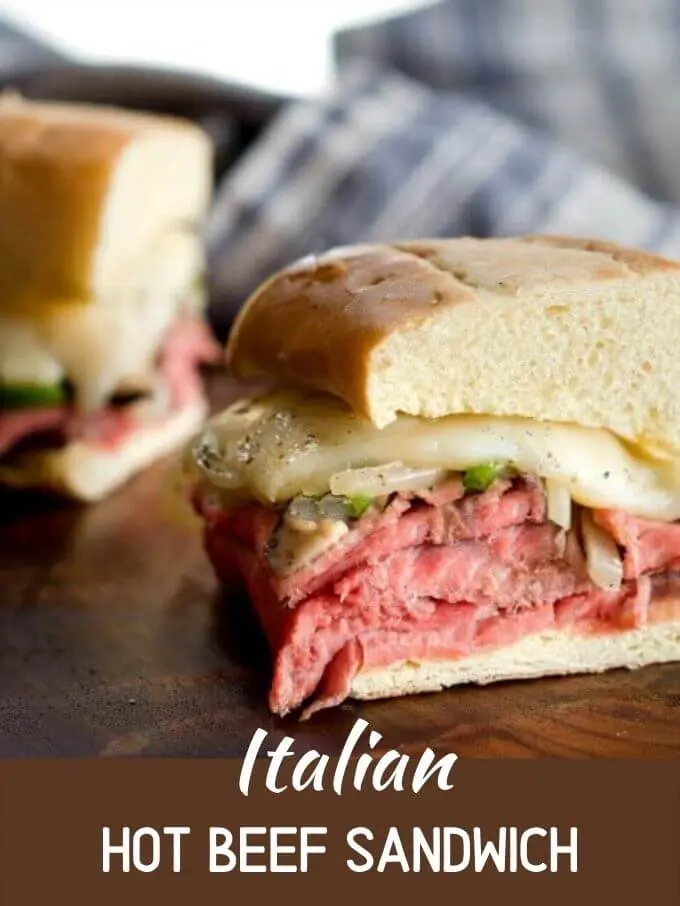 Close up photo of a sandwich heaped with rare prime rib, sauteed vegetables and italian seasoning on a wooden cutting board. Title Italian Hot Beef Sandwich is printed under the photo.