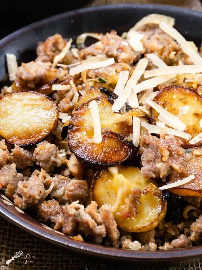 Top down photo of sausage and fried potatoes sprinkled with parmesan cheese in a brown bowl.