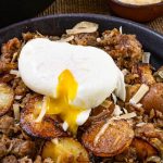 Top down photo of sausage and fried potatoes sprinkled with parmesan cheese with a soft cook egg pouring over it.