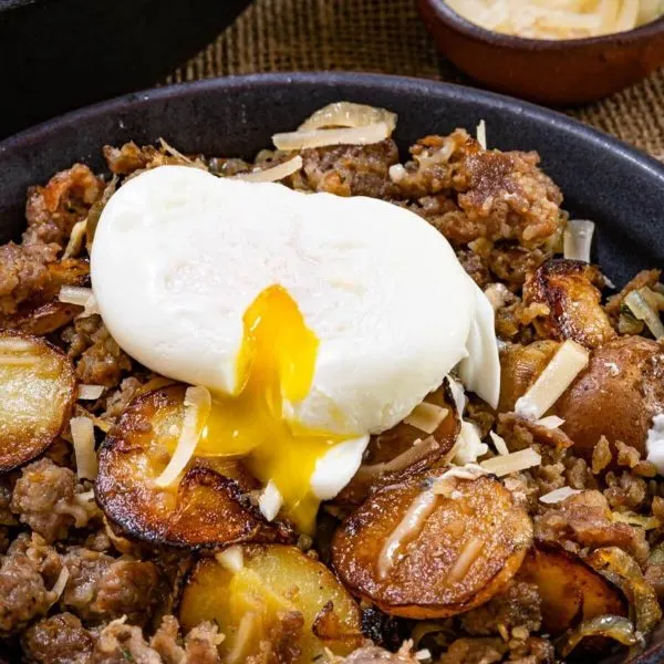 Top down photo of sausage and fried potatoes sprinkled with parmesan cheese with a soft cook egg pouring over it.