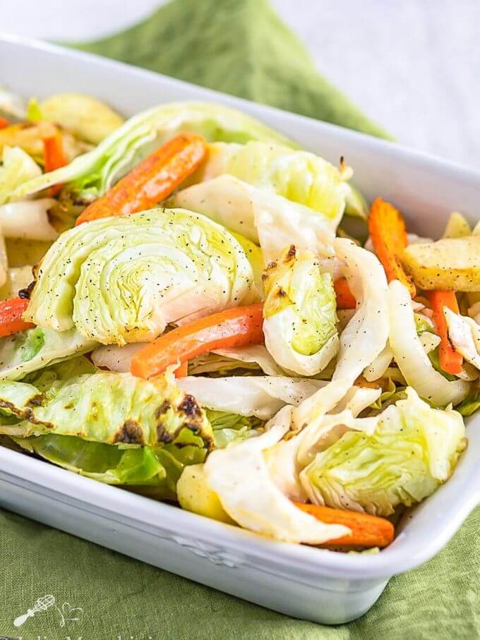White baking dish filled with golden roasted cabbage wedges, orange carrot pieces, and caramelized apple slices