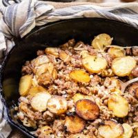 Angled view of Ground Sausage and fried potatoes in a black cast iron skillet with a serving spoon on the side