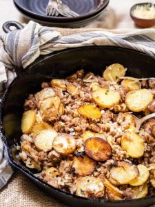 Angled view of Ground Sausage and fried potatoes in a black cast iron skillet with a serving spoon on the side