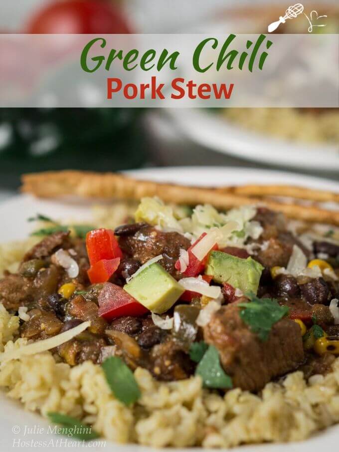 Close up angle view of a white plate layered with green tomatillo rice topped with chunks of pork, tomato, avocado, and cilantro with the title banner \"Green Chili Pork Stew\" across the top of the photo.