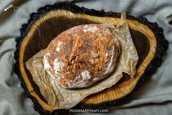 Top down photo of a loaf of beautifully browned spelt bread sitting on natural parchment paper and a wooden background.