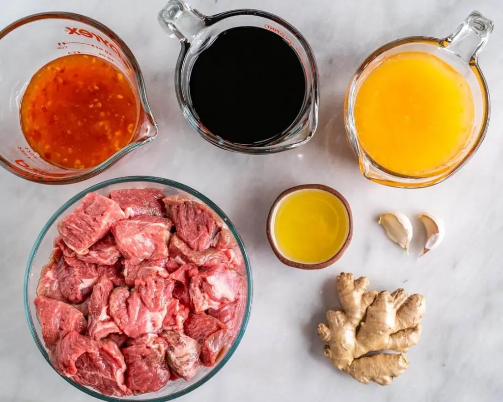 Bowls of raw chunks of lamb, fresh ginger, garlic, sweet chili, sauce, orange juice, soy sauce, and sesame oil.