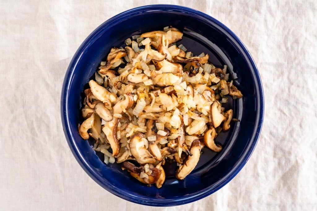 A blue bowl filled with sauteed onions and mushrooms over a white tablecloth.