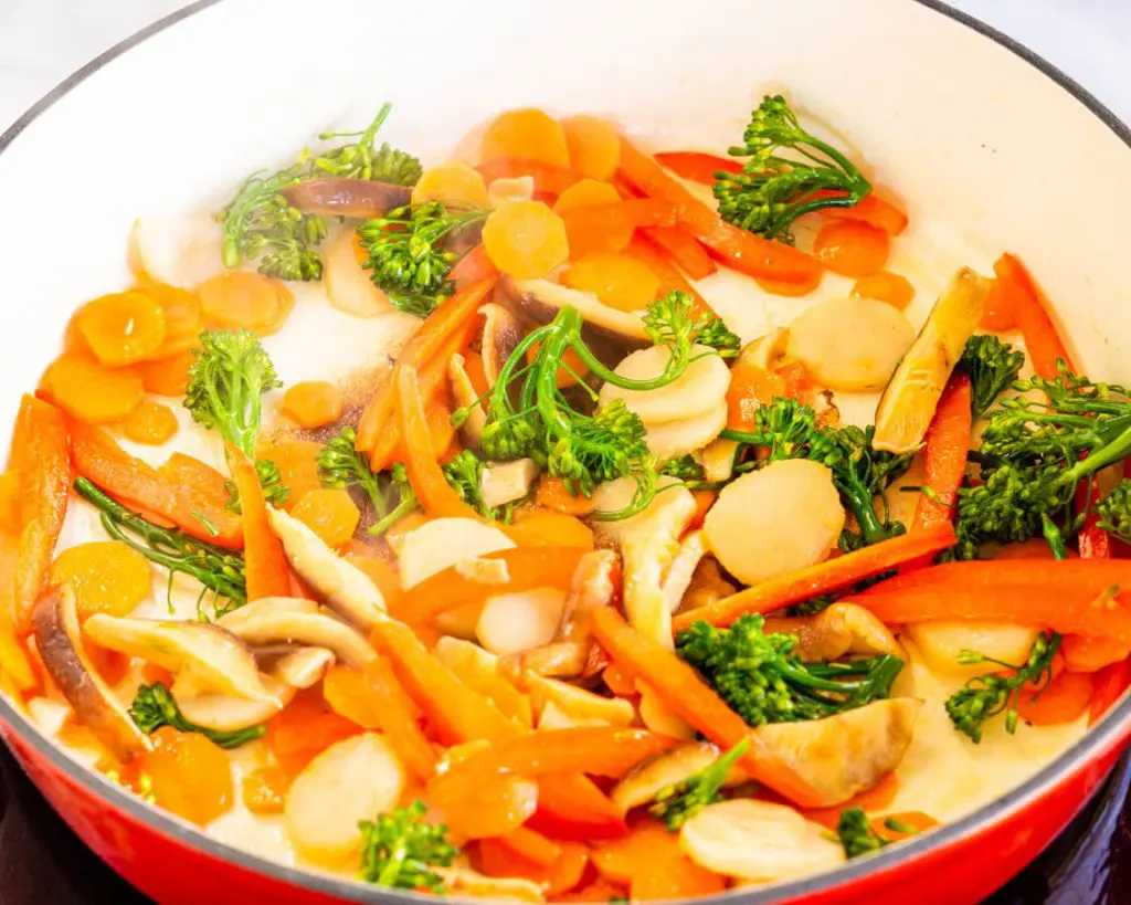 Red dutch oven filled with stir fry vegetables including carrots, water chestnuts, broccolini, and red peppers.