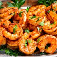 Silver serving platter heaped with spicy red blackened shrimp garnished with bright green Parsley.