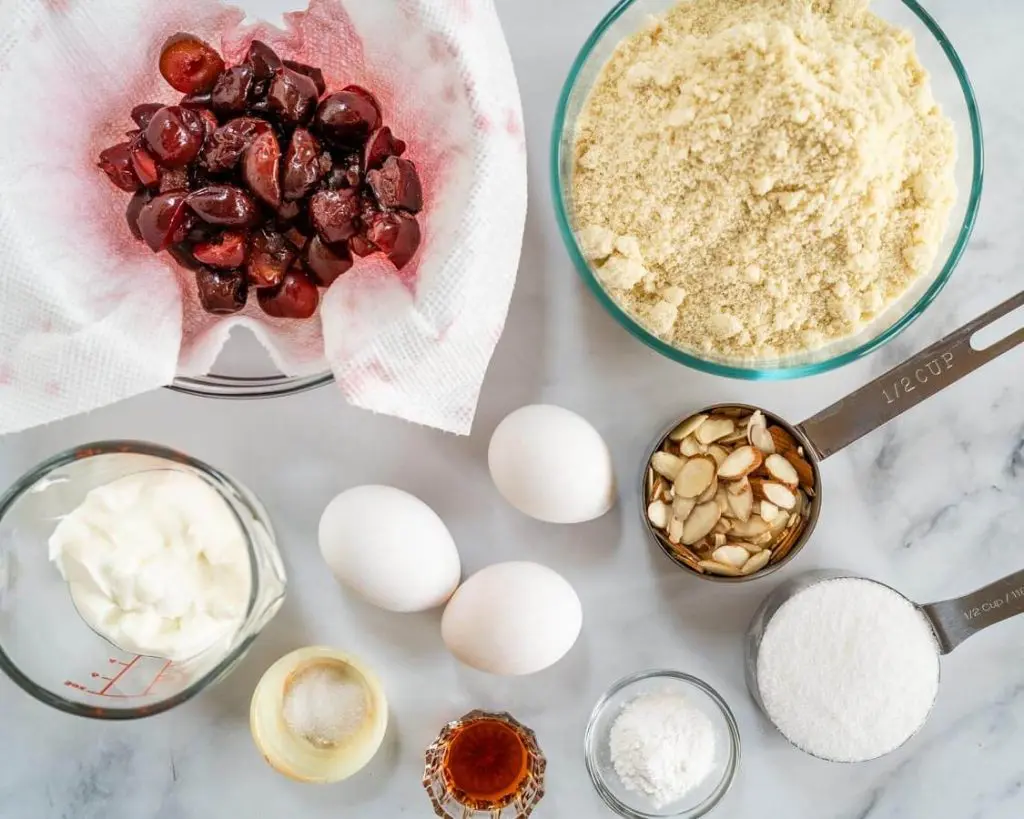 Ingredients used to make a Cherry Almond muffin including thawed cherries, sour cream, salt, eggs, vanilla, sugar, almonds, almond flour, and baking powder.