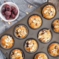 A top-down view of a tray of Cherry Almond Muffins and bowl of Frozen Cherries over a blue striped napkin.