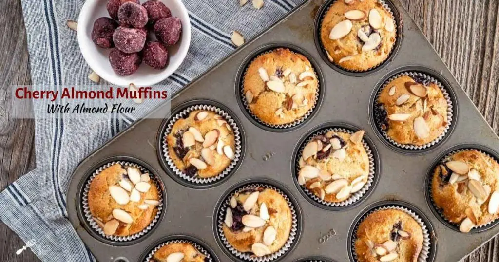 Top-down photo of a tray of Cherry Almond muffins over a striped napkin. A bowl of frozen cherries and the title of the recipe sit in the upper left.