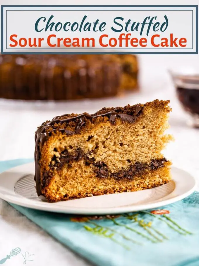 A side angle of a slice of Chocolate Coffee Cake on a white plate showing a layer of chocolate running through it and topped with streusel then drizzled with more chocolate. A pretty spring blue napkin sits below the plate and the cake sits behind it with a cup of coffee to the side. The title runs across the top of the photo.