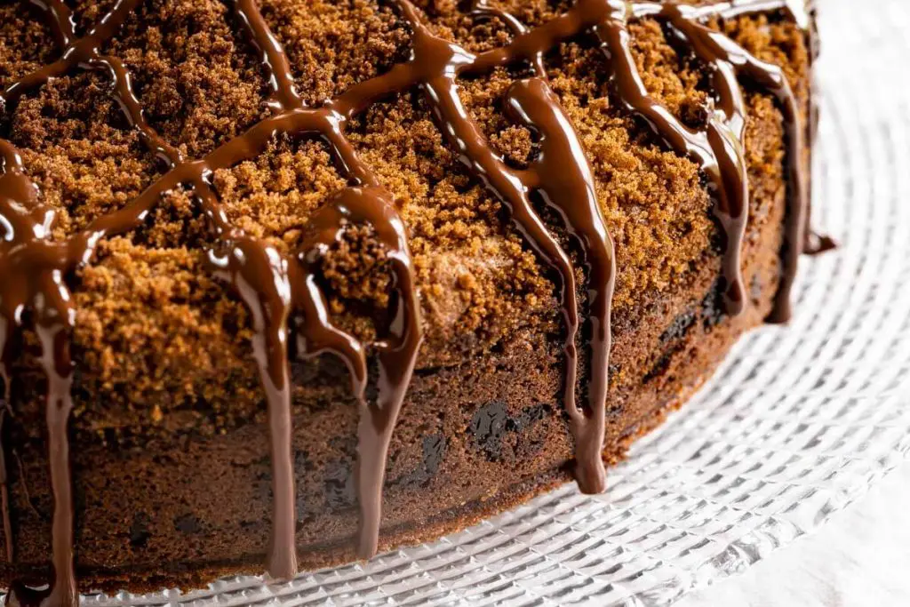 Side view of a cinnamon streusel coffee cake sitting on a glass plate drizzled with dark chocolate running down the sides. A layer of chocolate chips run through the middle of the cake.