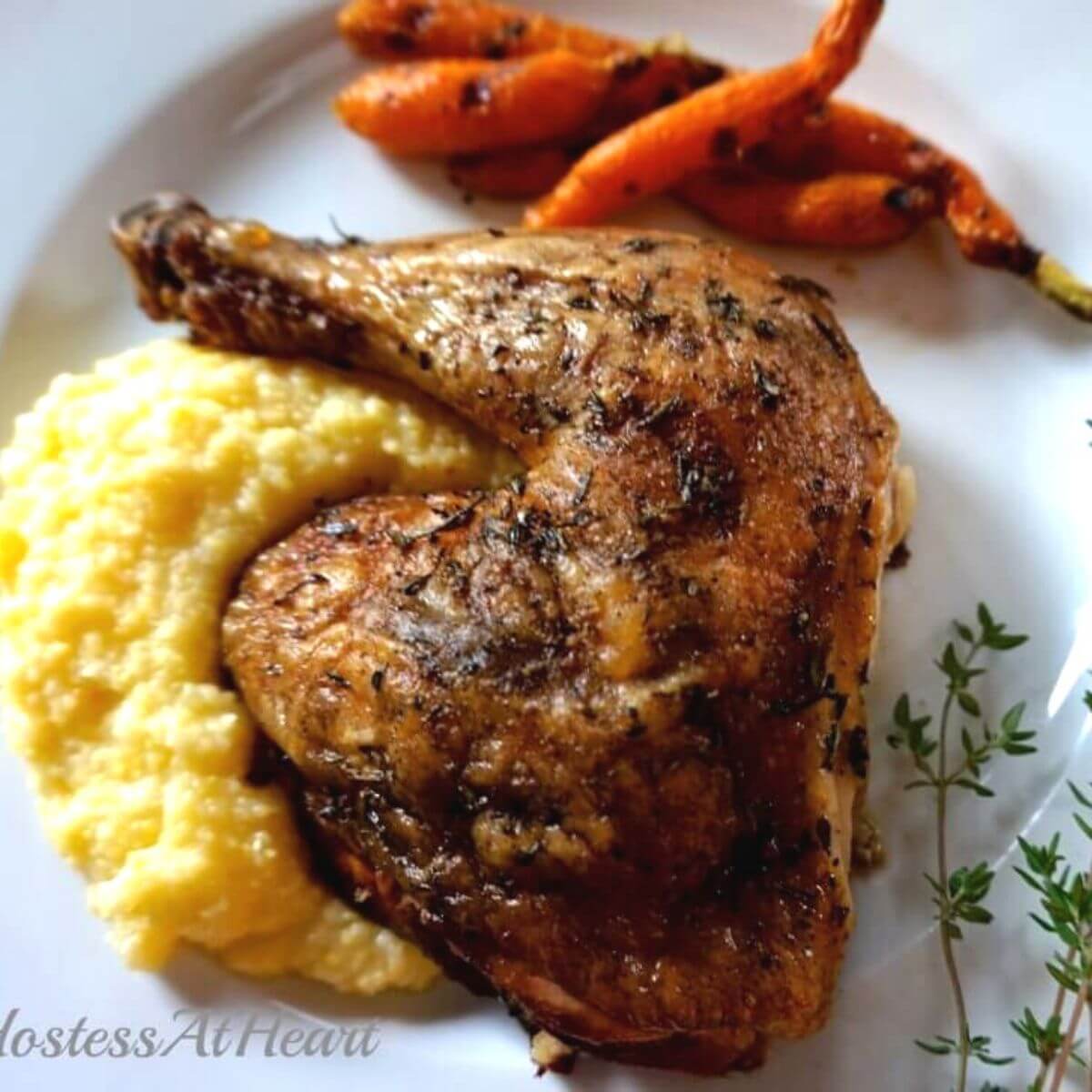 Top down view of a grilled chicken quarter laying on a bed of polenta on a white plate with a garnish of fresh thyme.