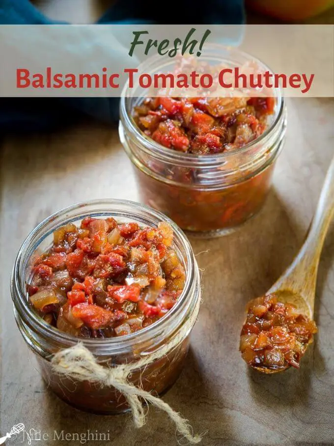 A wooden spoon filled with tomato chutney sits beside two jars filled with the tomato chutney on a wooden cutting board. The title \"Balsamic Tomato Chutney\" runs across the top of the photo.
