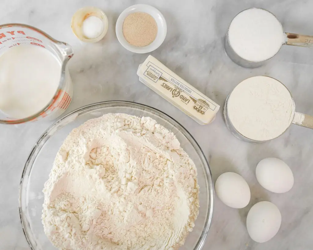 Ingredients used to make Kifli Walnut Rolls including flour, yeast, eggs, sugar, butter, salt, and milk in a large bowl.
