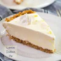 Close up side view of a slice of Lemon Icebox Pie. The slice has a thick graham cracker crust topped with a cool creamy layer and topped with a star of cool whip topping. The slice sits on a white plate over a blue napkin and the recipe title is in the left bottom corner.