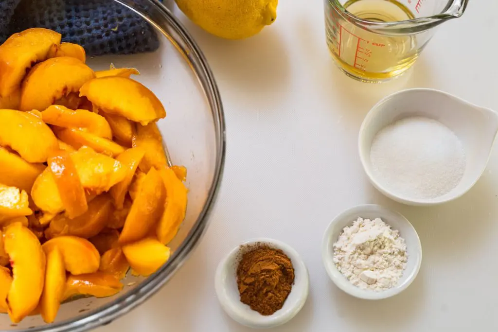 The ingredients used to make the peach filling in the peach crisp recipe including sliced peaches, cinnamon, flour, sugar, apple juice, and lemon juice.