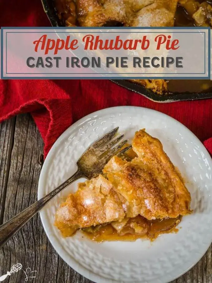 Top down photo of a slice of apple rhubarb pie on a white plate. An antique fork sits on the side of the plate. A partial view of the baked pie in a cast-iron skillet sitting over a red napkin is in the background. The title "Apple Rhubarb Pie Cast Iron Skillet recipe" runs across the top.