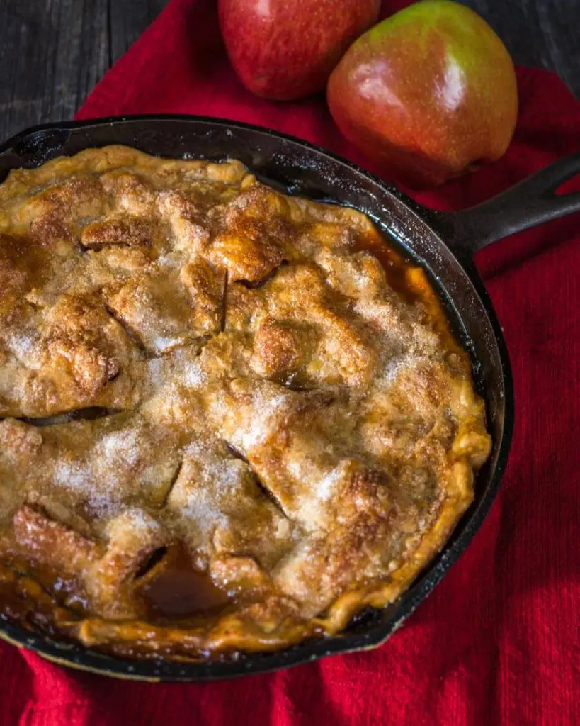 Top down view of an apple rhubarb pie baked in a cast-iron skillet sitting over a red napkin. Fresh apples are in the background.