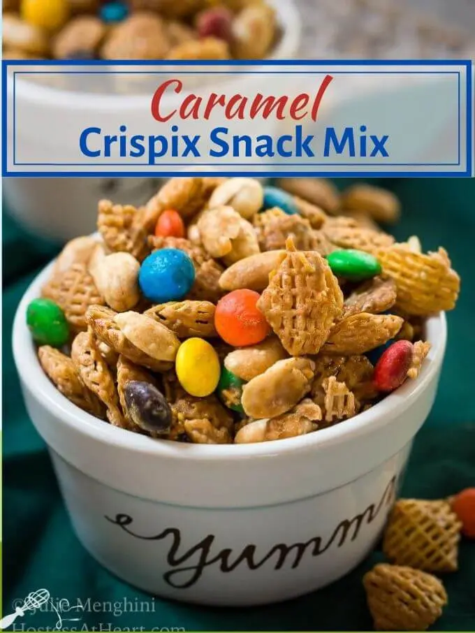 Top angle view of a white ramekin with the word yummy on the front filled with Caramel Crispix Snack Mix over a green napkin. Additional snack mix is sprinkled around the dish over the napkin. The title of the recipe runs across the top.