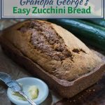 An angled loaf of bread with two fresh zucchini's sitting in the back. A white dish with butter and an antique knife sit in the front. The title "Grandpa George's Easy Zucchini Bread" runs across the top.