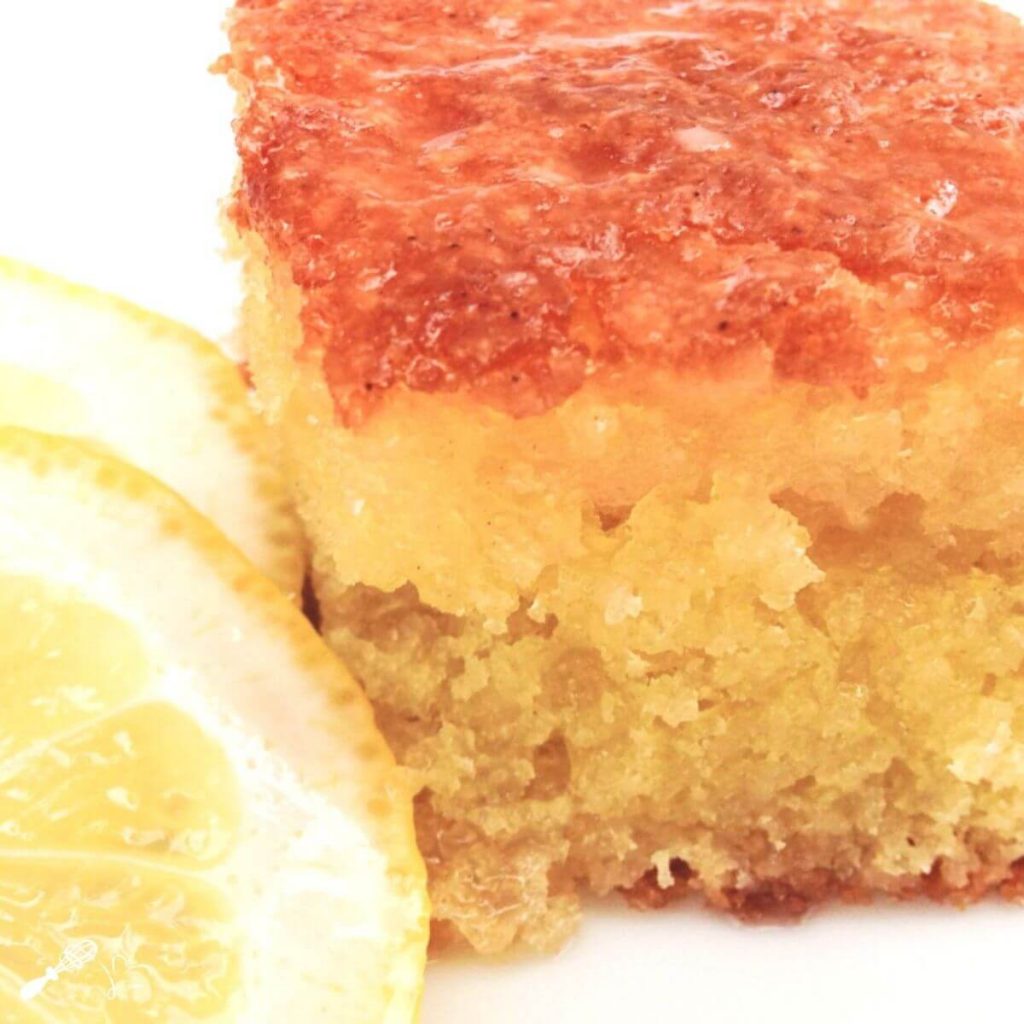 Front angled view of a piece of Lemon Olive Oil Cake with slices of fresh lemon sitting on the side.
