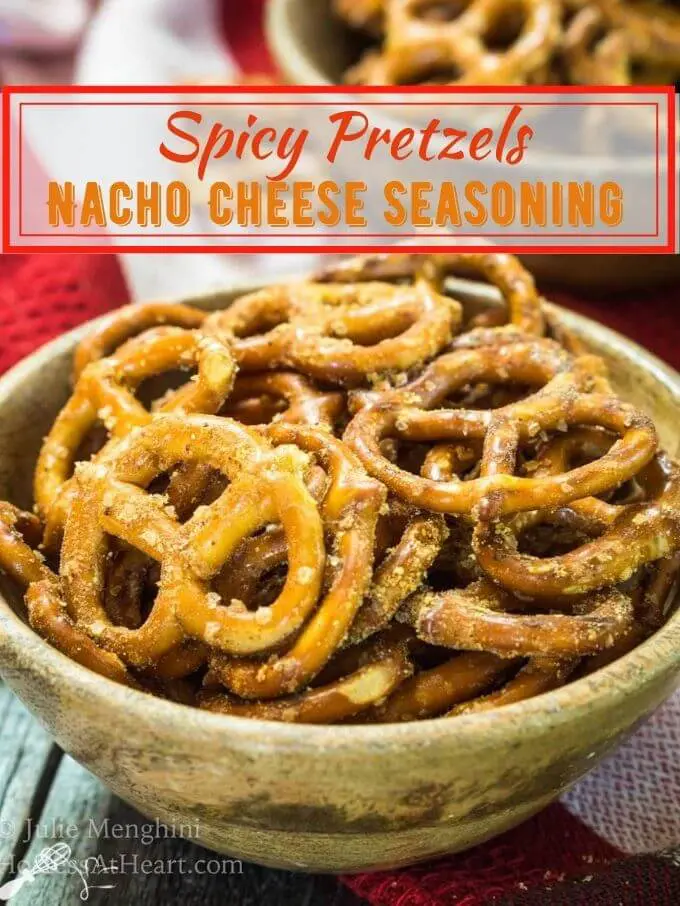 Side view of spicy pretzels, dotted with seasonings in a wooden bowl over a red checked napkin. The title "Spicy Pretzels Nacho Cheese Seasoning" runs across the top.
