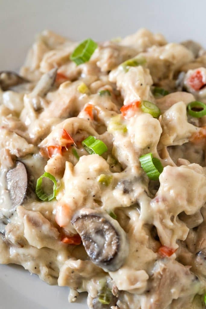 Close up of Turkey a la King on a gray plate shows chunks of turkey in a cream sauce dotted with red pepper, mushrooms, and green onion.