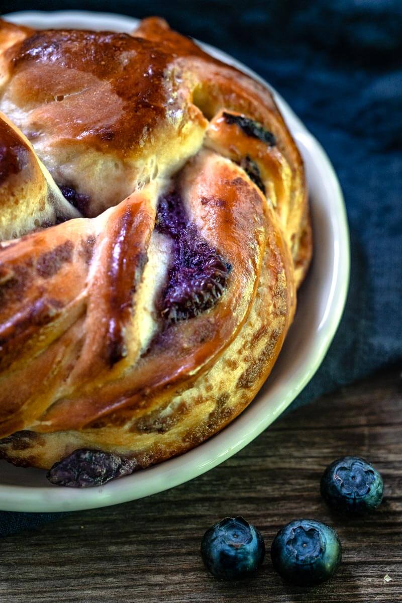 Close-up view of a Blueberry Twist Roll sitting on a white plate next to scattered blueberries.