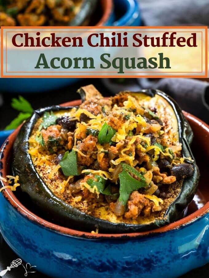 A baked half of an acorn squash brushed with chili powder and stuffed with chicken chili and garnished with cheese and cilantro sitting in a blue bowl with an adobe red edge. A second bowl sits in the background. The title "Chicken Chile Stuffed Acorn squash runs across the top.
