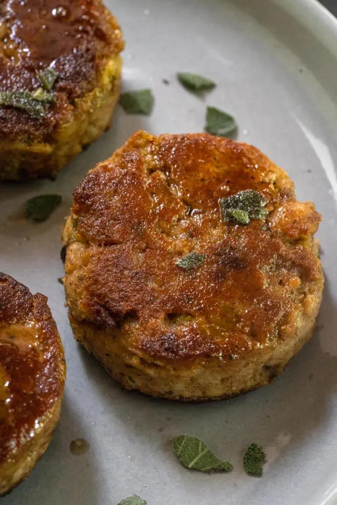Fried Dressing Pattie garnished with fresh sage on a gray plate. Two partial patties are on the side.