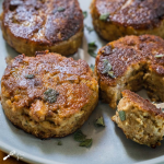 4 Fried Dressing Patties garnished with fresh sage on a gray plate. One Pattie has a fork-filled bite out of it.
