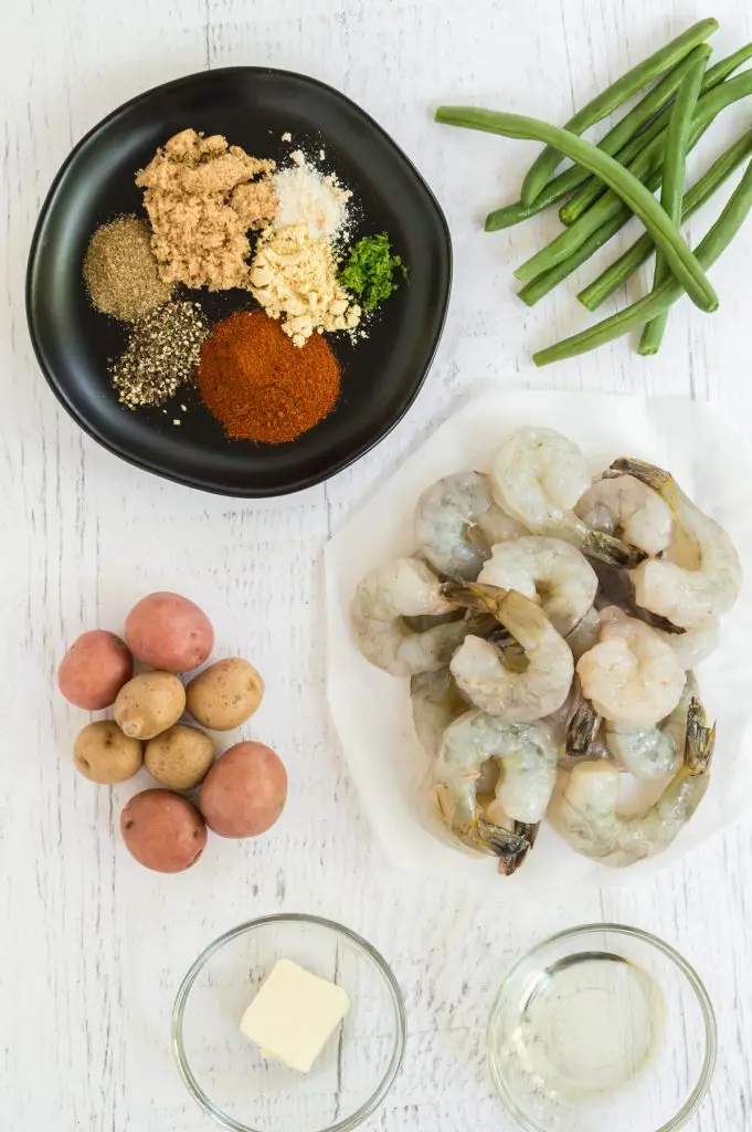 A bowl of spices, green beans, shrimp, potatoes & butter.