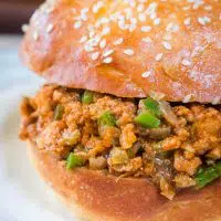 Close-up sideview of a turkey sloppy joe dotted with green pepper in a sesame seed bun sitting on a light blue plate.