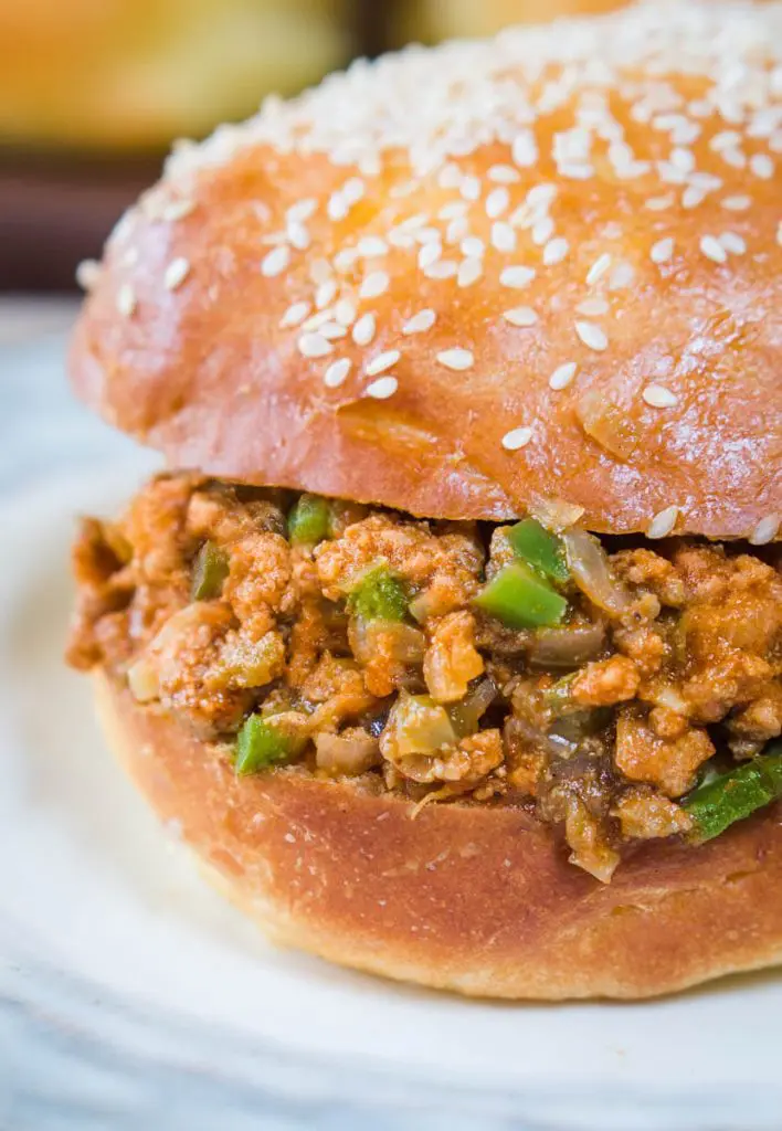 Close-up sideview of a turkey sloppy joe dotted with onion and green pepper on a sesame seed but sitting on a light blue plate.