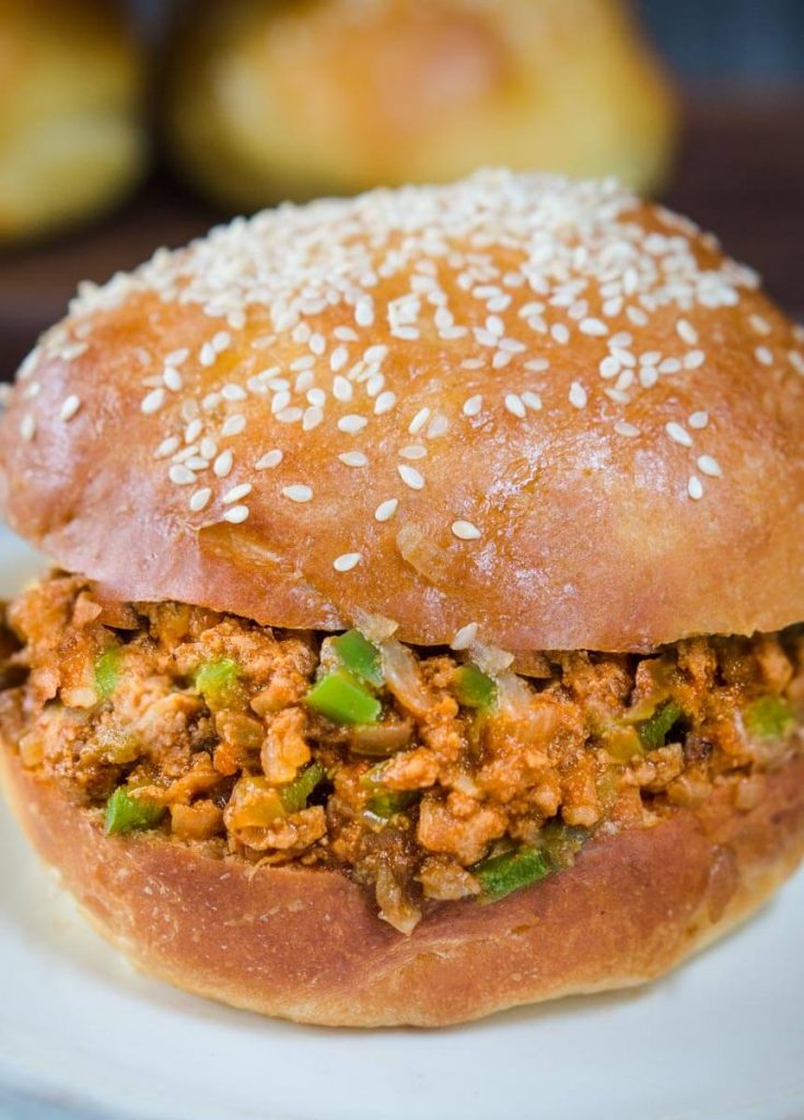 Top angle view of a turkey sloppy joe dotted with onion and green pepper on a sesame seed but sitting on a light blue plate.