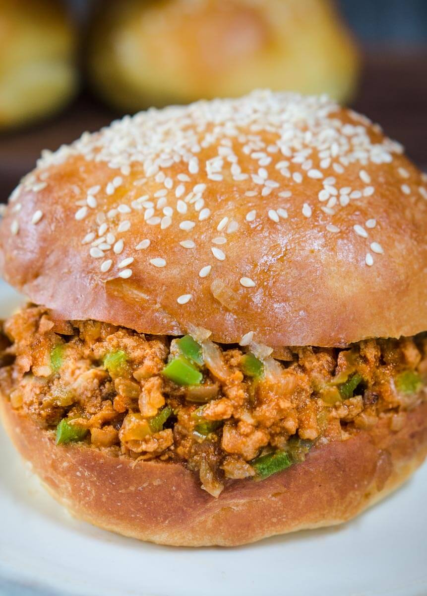 Top angle view of a ground turkey sloppy joe dotted with onion and green pepper on a sesame seed but sitting on a light blue plate.