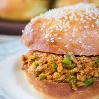 Sideview of a turkey sloppy joe dotted with onion and green pepper on a sesame seed but sitting on a light blue plate.