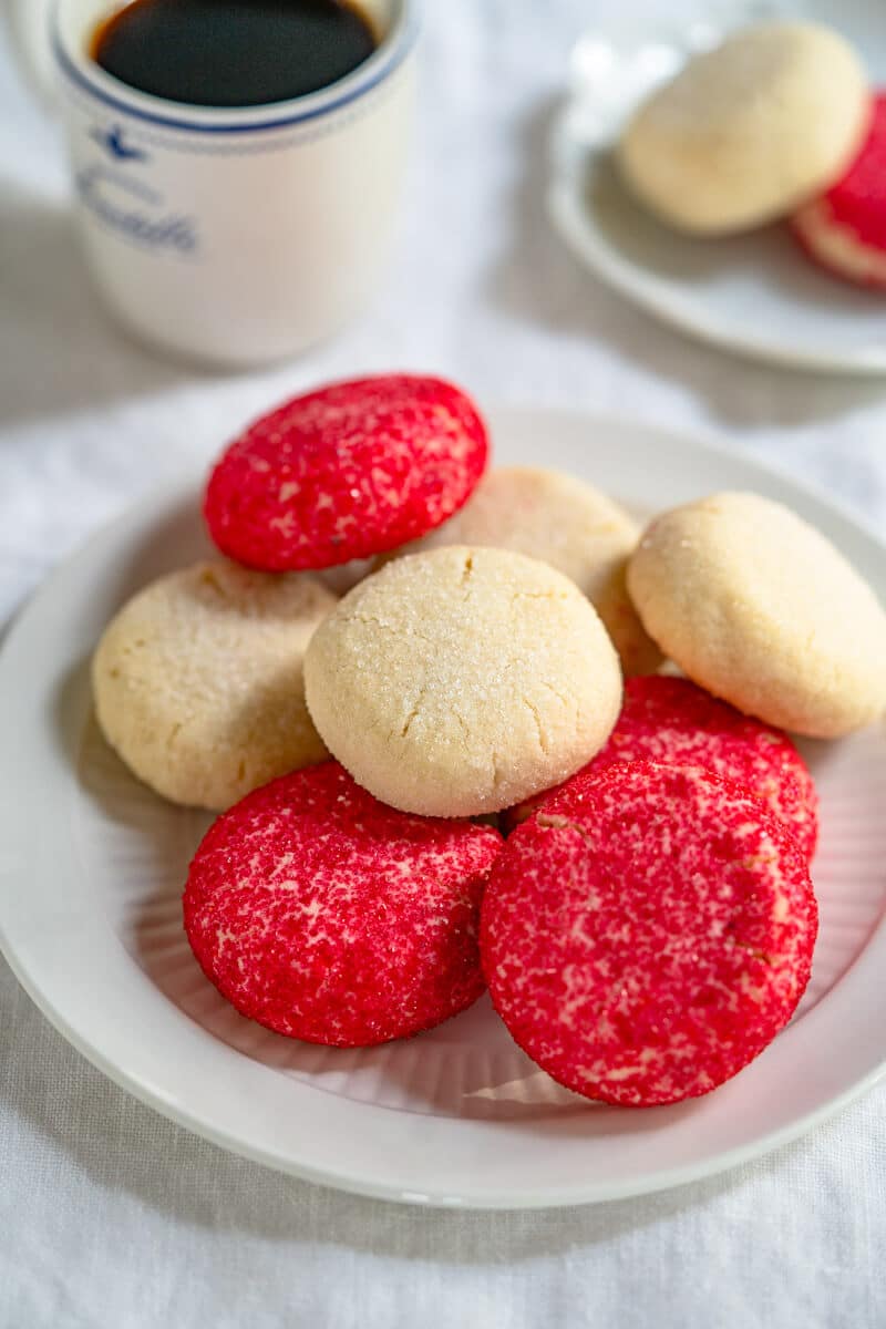 A plate of red and white decorated butter cookies with a cup of coffee and another plate holding two cookies in the background.