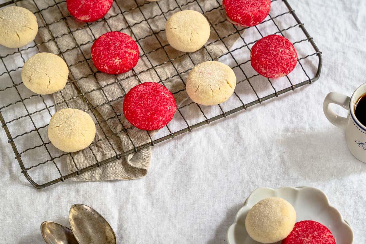 Top down view of a cooling rack filled with red and white butter cookies. A small plate of two cookies sit in the front next to two spoons.