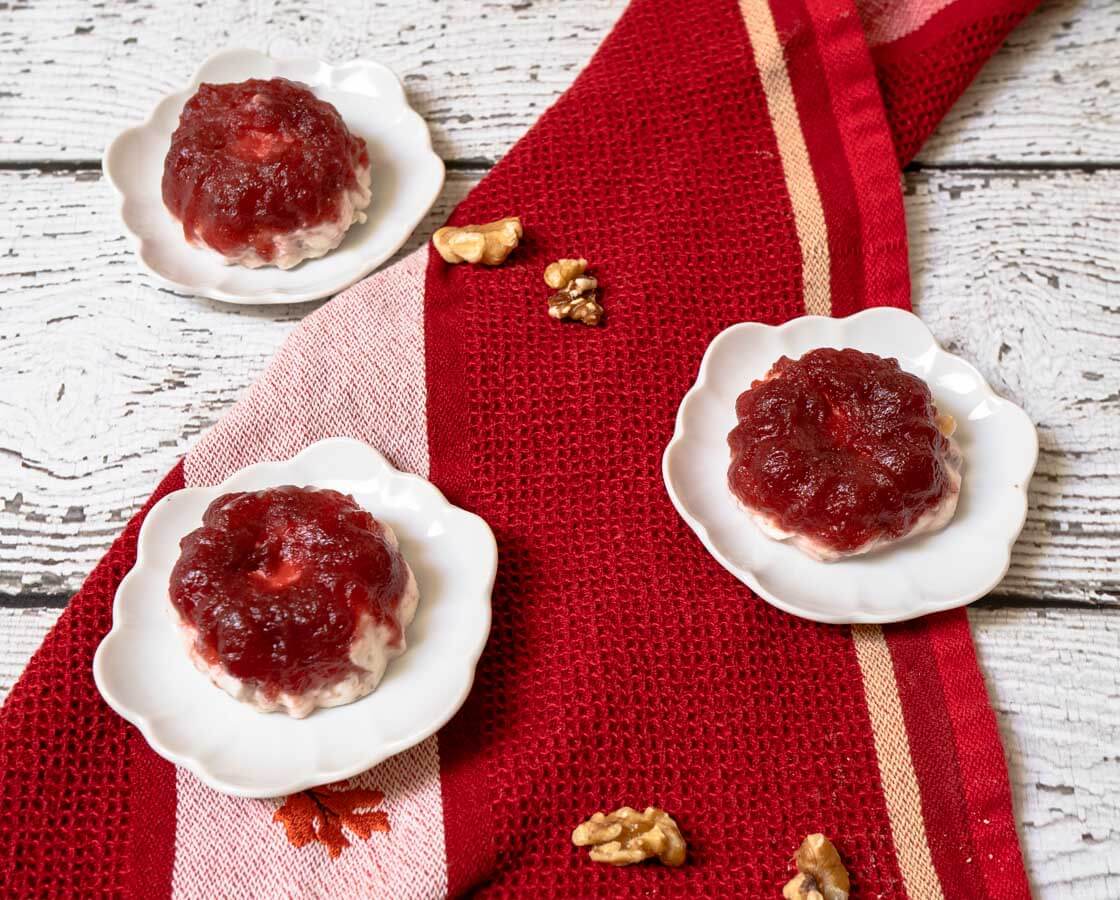 Top-down photo of three individual Frozen Cranberry Salads on small white plates over a red striped towel and walnuts scattered about.
